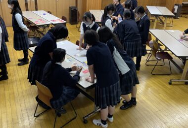 「どうしたらゴール達成し、世界の状況メーターもよくなるのだろう？」生徒たちはテーブル上のプロジェクトとカードとにらめっこしつつ、周りからの声掛けに反応…